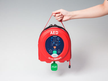 赤いAEDを手で持っています